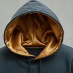 Closeup an oversized charcoal grey hoodie featuring a mustard yellow satin lining in the hood.