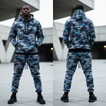 Product image showing the front and back of a stylish athletic sweatsuit in a blue and grey digital camouflage pattern, photographed in an urban environment.