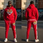 A bold red tracksuit featuring a hoodie and matching pants with white side stripes, embellished with chenille embroidered tiger graphics on the chest and the back of the joggers.
