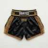 Back view of black Fairtex Muay Thai shorts featuring detailed traditional gold embroidery across the back and gold side panel accents.
