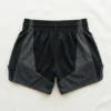 Back view of minimalist matte black Muay Thai shorts featuring clean white piping and a simple side split leg design.
