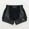 Front view of minimalist black Nak Muay Elite shorts with white drawstring ties, a small brand patch, and white outline trim.