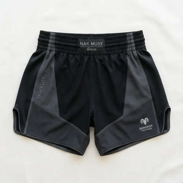 Front view of minimalist black Nak Muay Elite shorts with white drawstring ties, a small brand patch, and white outline trim.