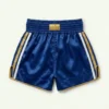 Back view of royal blue satin Muay Thai shorts featuring an embroidered tiger graphic and a gold traditional pattern on the left side.