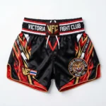 Front view of black Victoria Fight Club kickboxing shorts with an orange tiger graphic, gold waistband text, and red side accents.