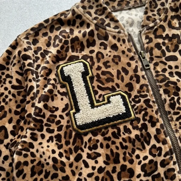 A closeup of leopard printed velour track jacket with chenille embroidered letter on chest.