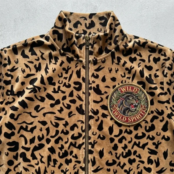 A closeup of leopard print velour track jacket with embroidered patch on the chest.