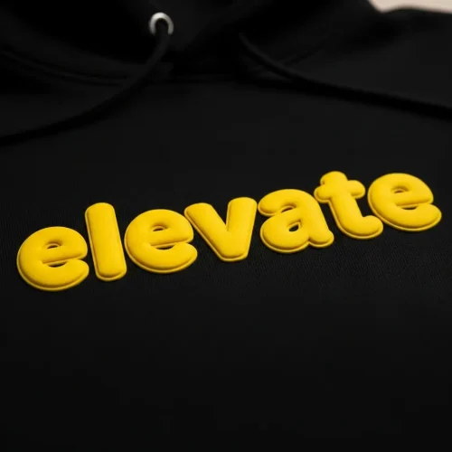 puff-printed-hoodie-closeup Black hoodie featuring the word "elevate" in bright yellow, showing the unique, soft, and inflated bubble texture of puff screen printing.